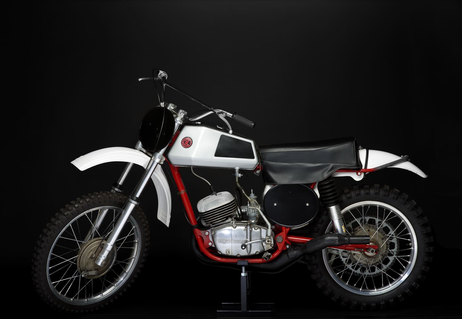 A white and red dirt bike on display against a black background.