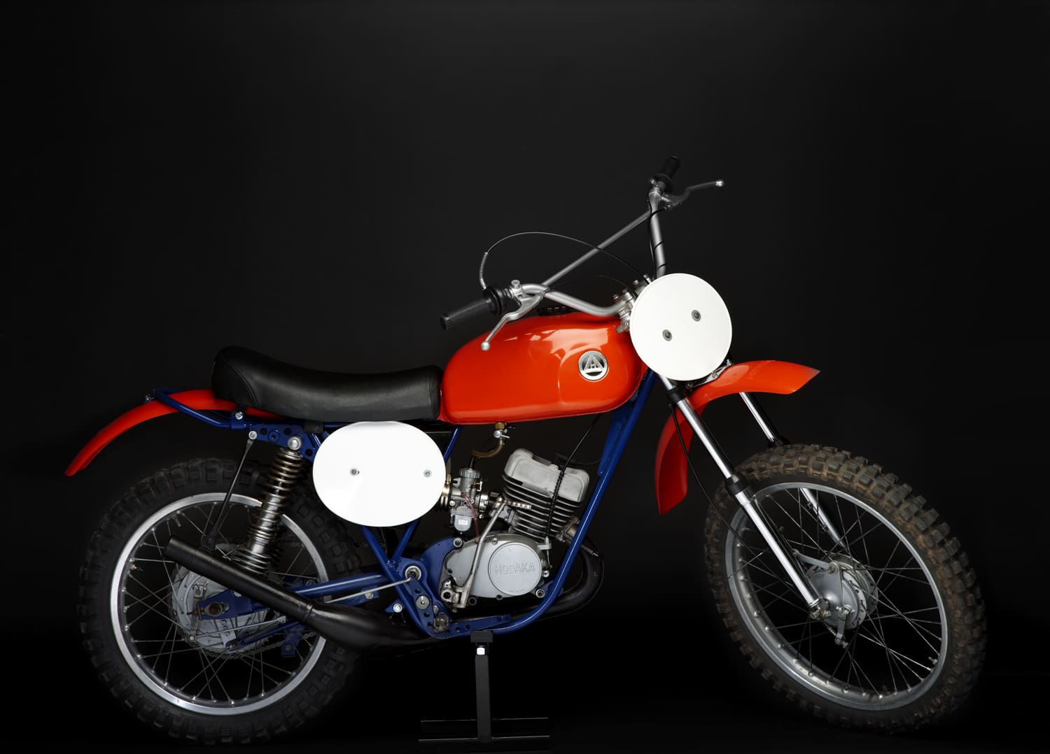 A red and blue dirt bike is on display against a black background.