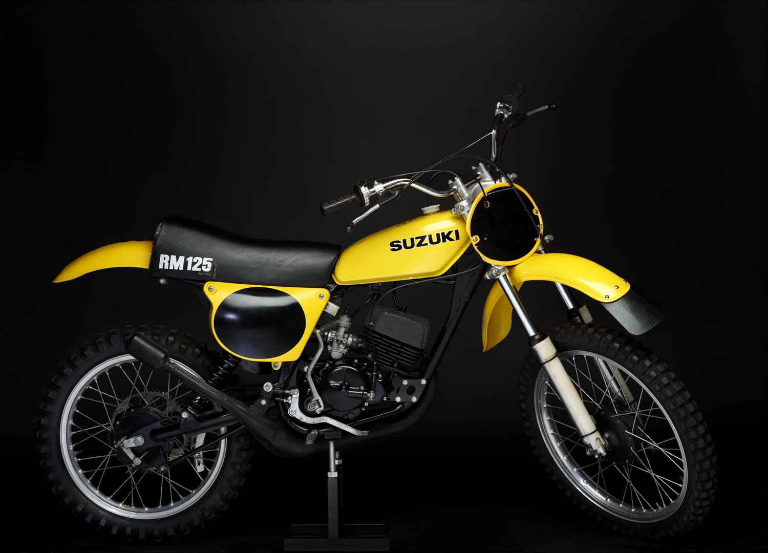 A yellow dirt bike on display against a black background.