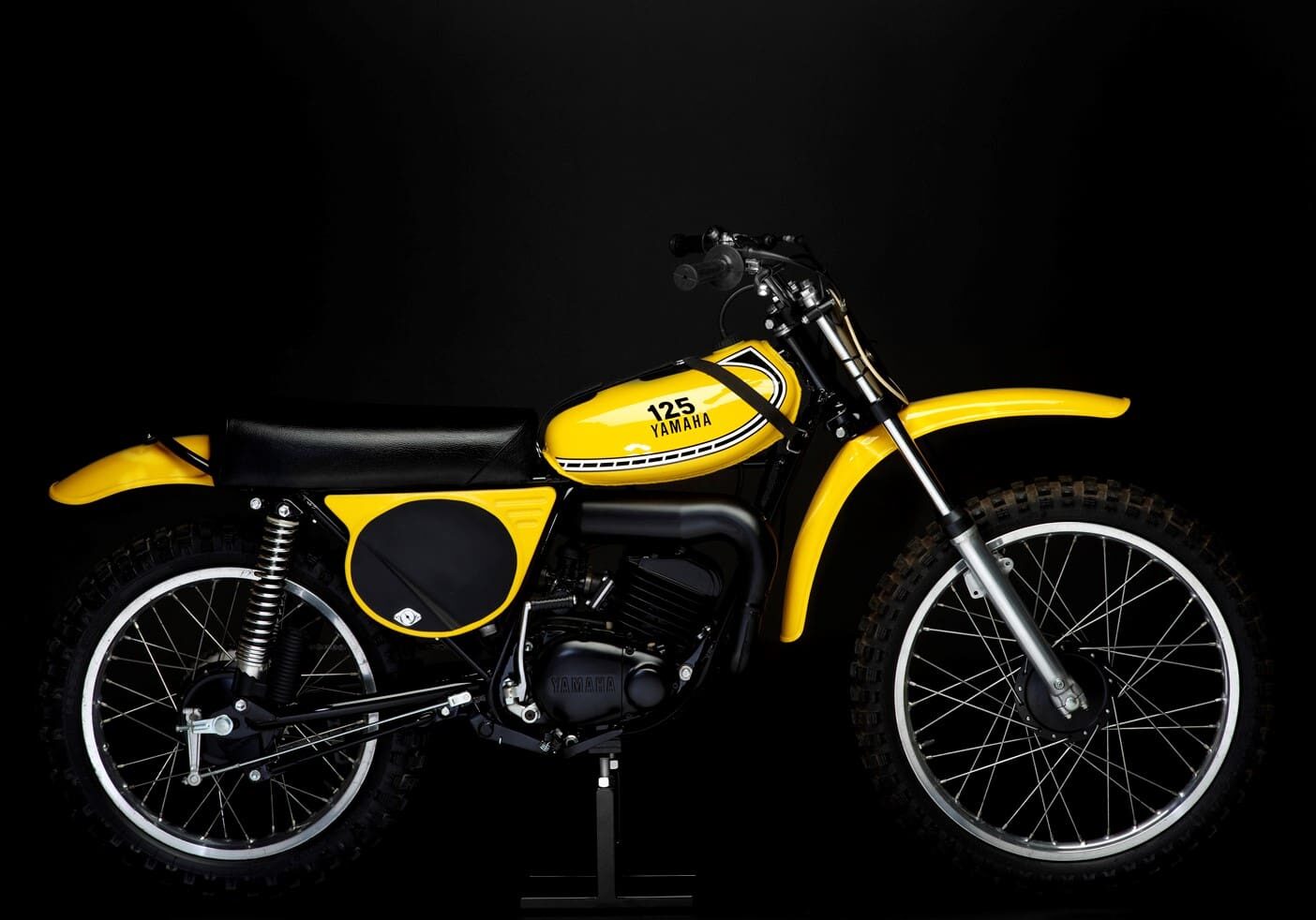 A yellow MX motorbike sits on a black background.